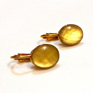 Puede incluir: Un par de pendientes de clip de tono dorado con piedras ovaladas de color amarillo translúcido.