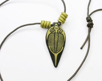 May include: A necklace with a green and black trilobite pendant and green beads. The necklace is made of brown cord.