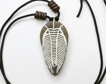 May include: A pendant necklace featuring a fossil design. The pendant is a light brown, oval-shaped stone with a white trilobite fossil design. The necklace has a black cord with wooden beads and a knotted closure.