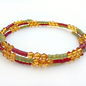 Puede incluir: Un brazalete de cuentas de tres hilos con cuentas rojas, verdes y ámbar. El brazalete está hecho con cuentas pequeñas y facetadas.