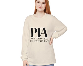 May include: Cream-colored long-sleeve shirt with the text "PIA THE TORTURED PTA DEPARTMENT" in black. The shirt is a neutral color and has a relaxed fit. The text is centered on the front of the shirt.