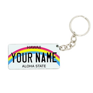 Könnte beinhalten: Ein weißer Schlüsselanhänger mit einem Regenbogen-Design und dem Text "HAWAII YOUR NAME ALOHA STATE".