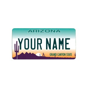 Könnte beinhalten: Arizona-Kennzeichen mit türkis-weißem Farbverlauf. Auf dem Schild steht oben "ARIZONA" und in fetten Buchstaben "YOUR NAME". Am unteren Rand befindet sich eine Wüstenlandschaft mit Sonnenuntergang und Kakteen.