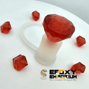 May include: A red, faceted, gem-like bottle stopper with glitter, attached to a white silicone loop. Several smaller red crystal-shaped objects are scattered around. The logo for Epoxy Emporium is visible at the bottom.