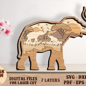 Peut inclure: Pièce d'art en bois en forme d'éléphant avec une scène de savane africaine. L'œuvre présente un coucher de soleil, des arbres et des animaux. Le texte "DIGITAL FILES FOR LASER CUT" est visible. La pièce mesure environ 30 cm de haut.