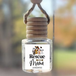 May include: A car air freshener with a white label that says "Rescue Mama" and features a group of dogs. The label also includes the text "Luv 4 Scents Co."