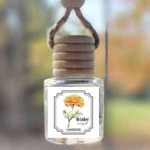 May include: A car air freshener with a wooden bead and string hanger. The bottle is clear and has a label with a yellow marigold flower and the text "October marigold".