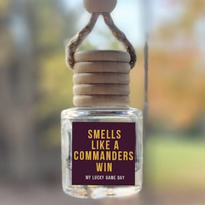 May include: A car air freshener with a burgundy and gold label that reads "Smells like a Commanders win. My lucky game day."
