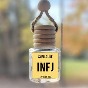 May include: A clear glass car air freshener with a wooden cap and a hanging string. The label reads "Smells Like INFJ" on a yellow background. The text "LUV4SCENTSCO." is at the bottom of the label.