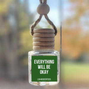 May include: A clear glass car air freshener with a wooden cap and a string for hanging. The label on the front reads "EVERYTHING WILL BE OKAY" in white text on a green background. The bottom of the label says "LUV4USCENTSCO."