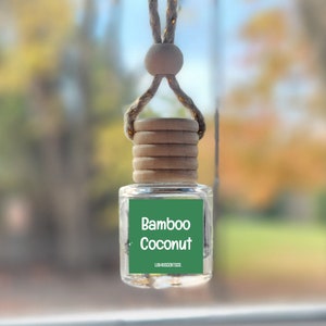 May include: A car air freshener hanging from the rearview mirror. The bottle is clear glass with a green label that reads "Bamboo Coconut" and "LILA ACCENTS CO."