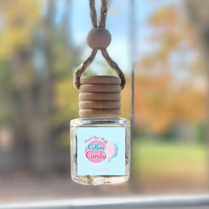 May include: A car air freshener with a light blue bottle and a white label that says "Sweet, Soft & Fluffy Cotton Candy". The bottle is hanging from a brown string with wooden beads.