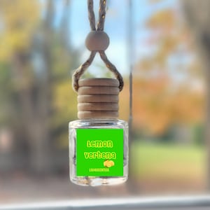 May include: A green and yellow car air freshener with a wooden top and a string for hanging. The label reads "Lemon Verbena" and "Luv-A-Scents Co."
