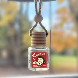 May include: A car air freshener with a red and white label that says "Coffee! You can sleep when you're dead!" The label features a retro illustration of a woman holding a cup of coffee.