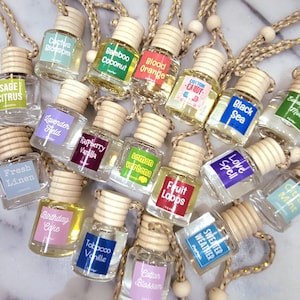 May include: A collection of 18 small glass bottles with wooden caps and string hangers. Each bottle contains a different scented oil and has a label with a different scent name. The scents include: Sage Citrus, Cactus Blossom, Bamboo Coconut, Blood Orange, Cotton Candy, Black Sea, Lavender Held, Raspberry Vanilla, Lemon Verbena, Fruit Loops, Love Spell, Fresh Linen, Birthday Cake, Tobacco Vanille, Cotton Blossom, and Sweater Weather.