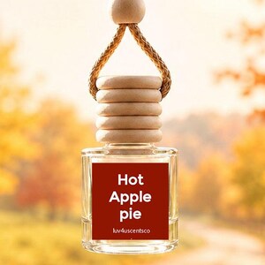 May include: A clear glass car air freshener bottle with a light wood cap and a braided tan cord for hanging. The bottle features a square red label with the white text Hot Apple Pie and luv4uscentsco printed in a smaller font at the bottom.