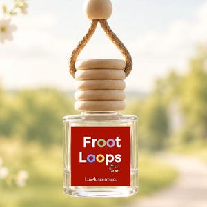 May include: A small, clear glass car air freshener bottle with a wooden cap and a tan hanging cord. The bottle features a square red label with the white text Froot Loops, a small colorful cereal graphic, and the text Luv4uscentsco in white.