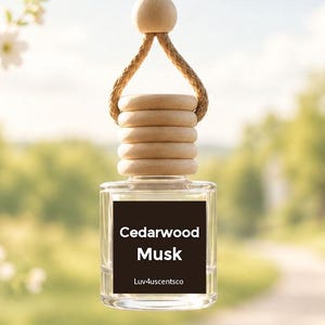 May include: A clear glass car air freshener bottle with a square base and a light wood cap. A brown label on the front features the white text Cedarwood Musk and Luv4scentsco. The bottle hangs from a tan braided rope with a round wooden bead.