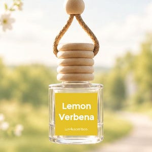 May include: A small clear glass bottle hanging from a tan rope with a wooden bead and a ribbed wooden cap. The bottle features a yellow square label with the white text Lemon Verbena and the smaller text luv4scentsco. centered below it.
