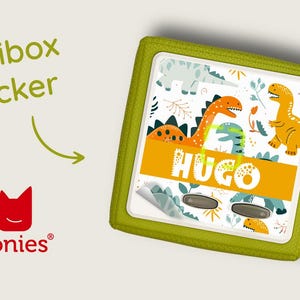 May include: A green Toniebox sticker with a dinosaur theme. The sticker features a yellow, orange, and green dinosaur design with the name "Hugo" printed in yellow letters.