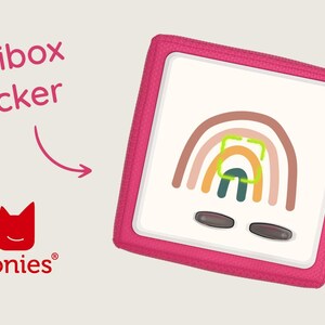 May include: Pink Toniebox with a rainbow sticker on the front. The sticker is a multi-colored rainbow with a green, orange, and brown design. The Toniebox has two buttons on the front.
