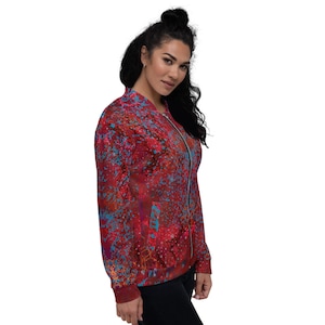 May include: A red, blue, and orange patterned bomber jacket with a zipper closure. The jacket has a  distressed look with a splattered paint effect.
