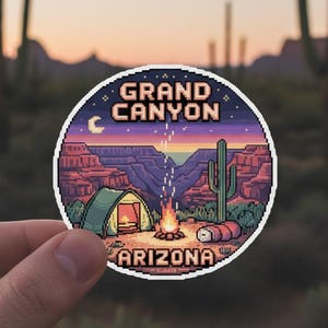 May include: A circular sticker depicting a pixelated Grand Canyon scene at dusk. The design includes a tent, campfire, cactus, and the text "Grand Canyon Arizona". The sticker is held in a person's hand.