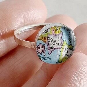 May include: A silver ring with a round glass cabochon featuring a vintage map of Europe. The map shows the countries of France, Spain, Belgium, Ireland, and England. The cities of Paris, London, Madrid, Dublin are labeled on the map.