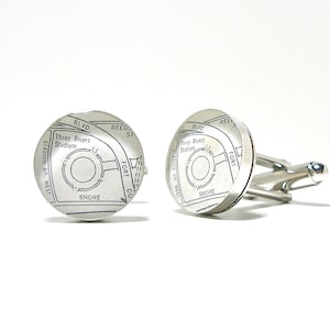 May include: Silver cufflinks with a map design featuring the text "Three Rivers Stadium", "Stadium Dr. West", "Shore", "Fort Du", and "Blvd". The cufflinks have a circular face and a silver backing.