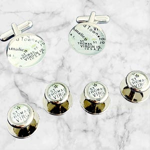 May include: A set of silver cufflinks and shirt studs. The cufflinks and studs have a circular design with a map of St. Thomas, Virgin Islands, and the text "St. Thomas Virg." on them.
