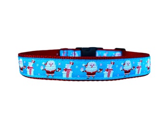 Pode incluir: Coleira vermelha para cão com um padrão azul e branco de Papai Noel segurando presentes. A coleira tem uma fivela de plástico preta.