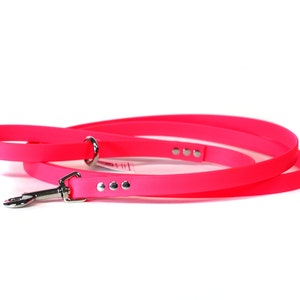 May include: A bright pink dog leash with a silver clip and three silver dots. The leash is coiled and ready for use.