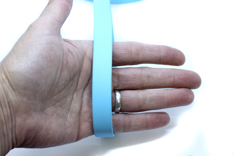 May include: A light blue leather strap, approximately 1 inch wide, is held in a person's hand. The strap is smooth and appears to be made of high-quality leather.