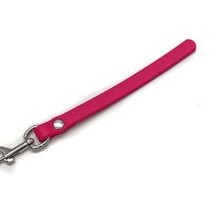 Puede incluir: Una correa de cuero rosa con un clip de metal plateado.