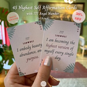 May include: Two affirmation cards are held in a hand, featuring text and decorative elements. The cards, measuring 2x2.9 inches, have the text "I embody beauty, abundance, and purpose" and "I am becoming the highest version of myself every single day."