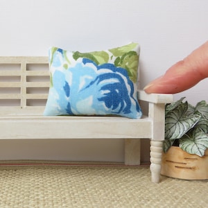 May include: A white bench with a blue and green floral patterned pillow. The bench has turned legs and is sitting on a woven rug.