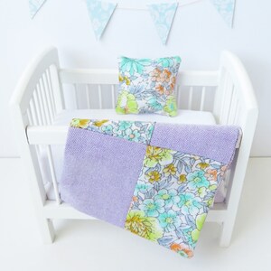 May include: A white cot with a purple and floral patterned quilt and a floral pillow. The cot is decorated with blue and white bunting.