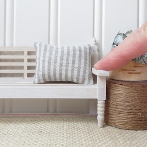 Peut inclure: Un banc miniature blanc avec des pieds tournés et un coussin rayé gris et blanc. Le banc est posé sur un tapis beige.
