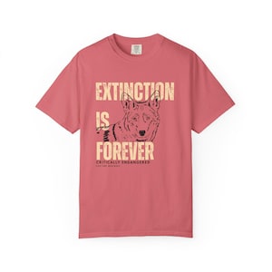 Op de afbeelding: Een roze t-shirt met een wolf illustratie en de tekst "EXTINCTION IS FOREVER" in een vintage lettertype. De tekst "CRITICALLY ENDANGERED" en "SAVE THE RED WOLF" staan ook op het shirt.