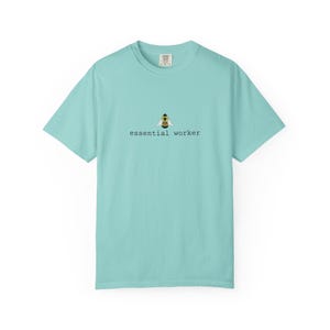 May include: A light blue t-shirt with the words "essential worker" printed in a black, sans-serif font. Above the text is a small graphic of a bee wearing a hard hat. The shirt is a crew neck and has short sleeves.