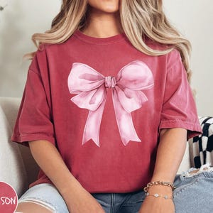 Pink Bow T-Shirt, Cute Pink Ribbon Graphic Tee, Feminine Bow Shirt, Casual Stylish Top, Fashionable Gift for Women, Sweet and Chic Tee Gift