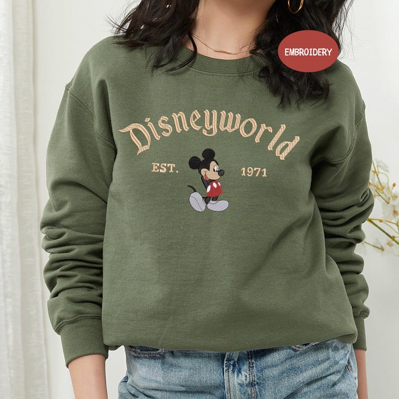 A woman wearing a green sweatshirt with the Disneyworld logo and text.