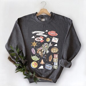 A gray sweatshirt with a colorful graphic design featuring characters from the Toy Story franchise, including Buzz Lightyear, Woody, and other iconic figures.