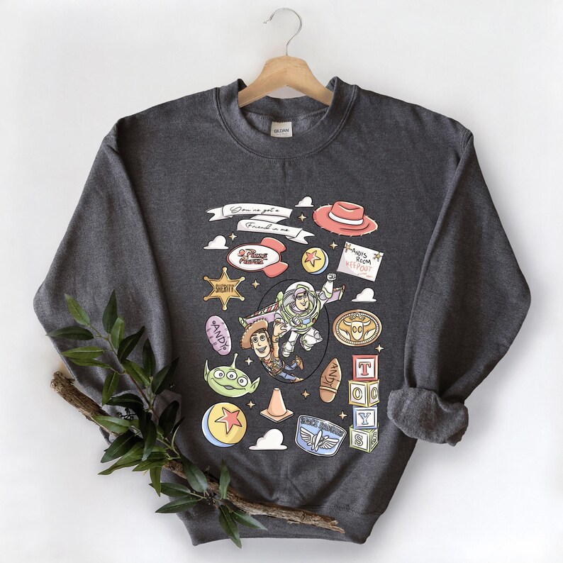 A gray sweatshirt with a colorful graphic design featuring characters from the Toy Story franchise, including Buzz Lightyear, Woody, and other iconic figures.