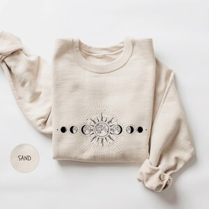 A beige sweater with a graphic design depicting the phases of the moon and sun on the front.