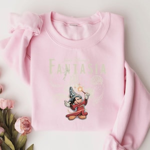 A pink sweatshirt with a Disney-themed graphic of Mickey Mouse and a wizard on it.
