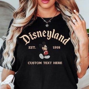 A woman wearing a black t-shirt with the text "Disneyland EST. 1955" and a Mickey Mouse graphic, along with the text "CUSTOM TEXT HERE".
