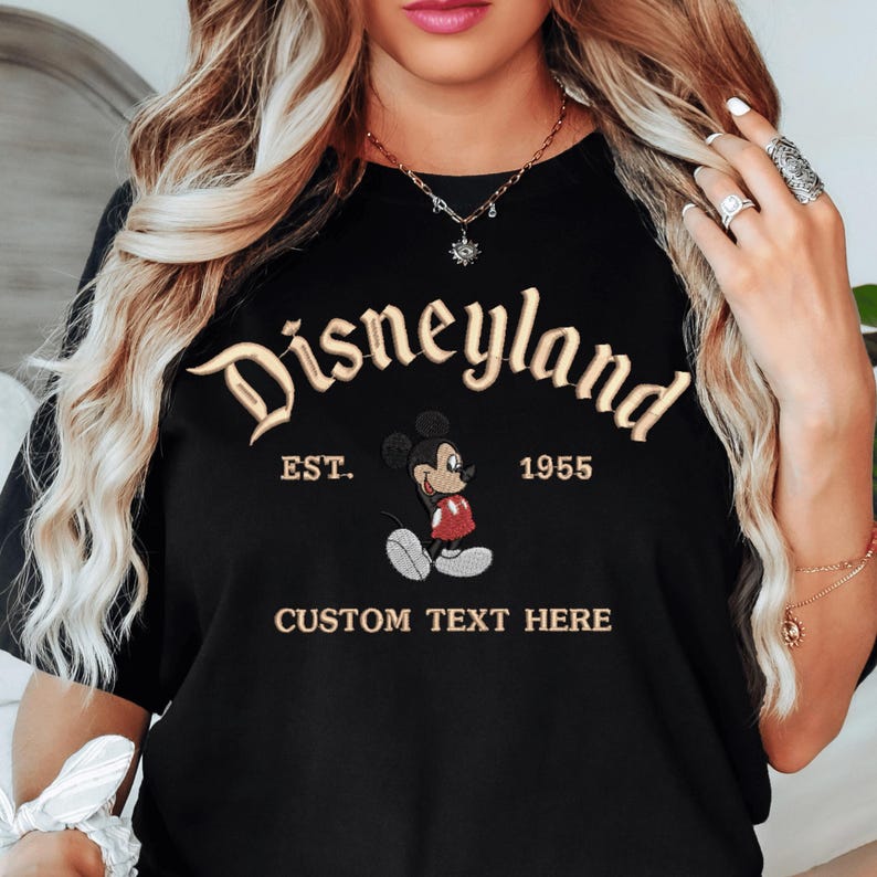 A woman wearing a black t-shirt with the text "Disneyland EST. 1955" and a Mickey Mouse graphic, along with the text "CUSTOM TEXT HERE".