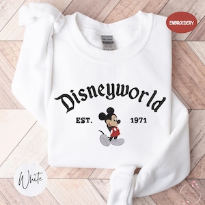 A white t-shirt with the text "Disneyworld" and a Mickey Mouse graphic printed on it, along with the text "EST. 1971" below the Mickey Mouse.