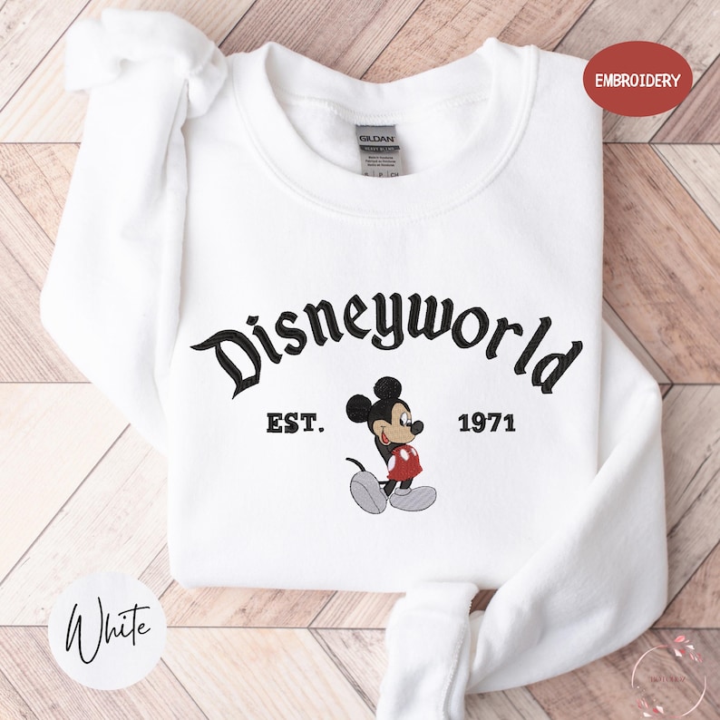 A white t-shirt with the text "Disneyworld" and a Mickey Mouse graphic printed on it, along with the text "EST. 1971" below the Mickey Mouse.